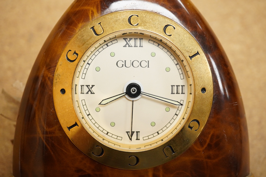 A Gucci gilt and enamelled stirrup shaped alarm clock with plaited and tasselled leather decoration, 9cm high